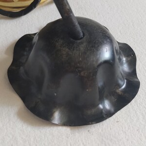 May include: Close-up of a dark, possibly antique, metal ceiling fixture component. The piece has a scalloped edge and a central hole for a rod. The finish appears aged with some wear.
