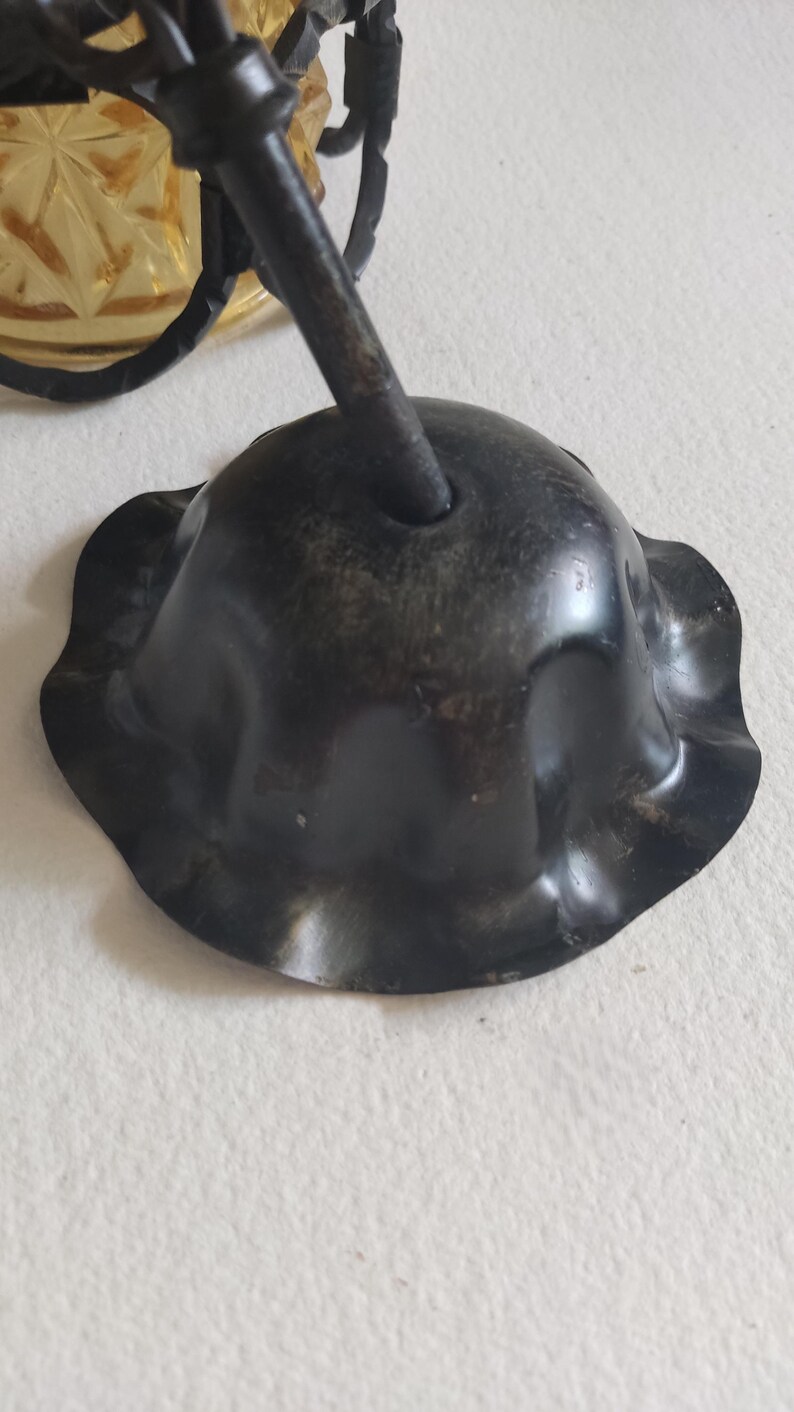May include: Close-up of a dark, possibly antique, metal ceiling fixture component. The piece has a scalloped edge and a central hole for a rod. The finish appears aged with some wear.