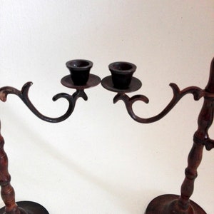 May include: A pair of antique brass candle holders with wooden bases. Each holder has a curved arm with a cup for a candle. The holders are connected by a decorative metal bar.