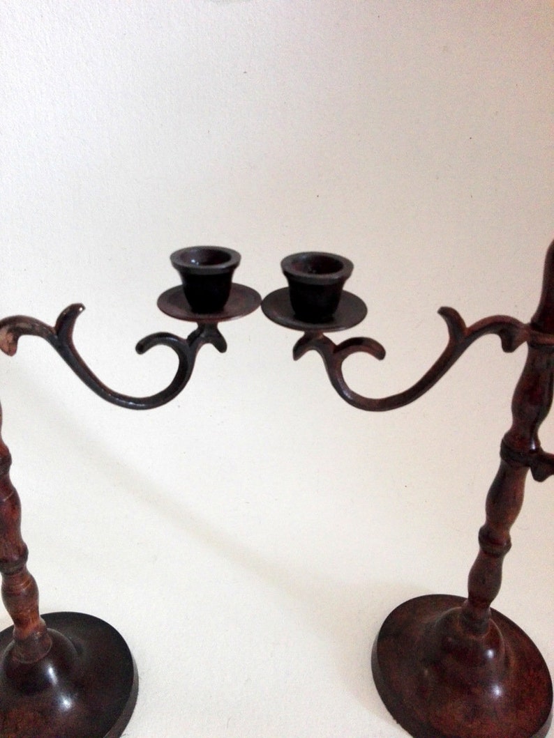 May include: A pair of antique brass candle holders with wooden bases. Each holder has a curved arm with a cup for a candle. The holders are connected by a decorative metal bar.