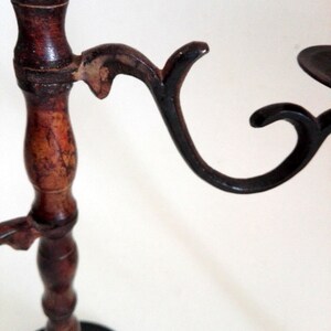 May include: A wooden candle holder with three black metal candle arms. The candle holder has a dark brown finish and a round base.