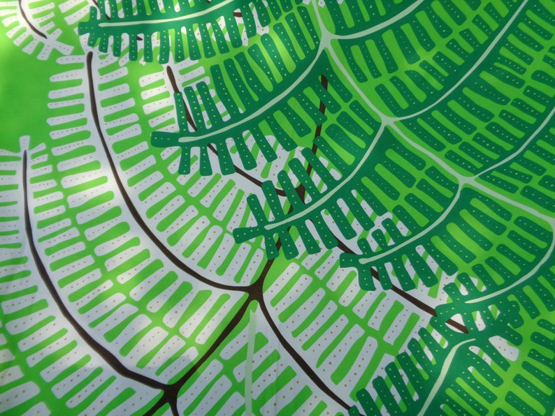 May include: A close-up of a fabric with a repeating pattern of green and white fern-like shapes on a bright green background. The design features detailed leaf structures with brown stems, creating a natural, botanical theme.