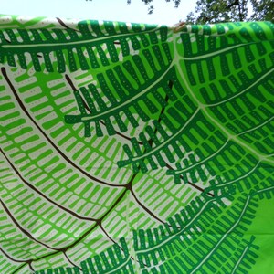 May include: A bright green fabric featuring a repeating pattern of fern leaves in green, white, and brown. The design creates a sense of depth and movement, suitable for home decor or clothing.