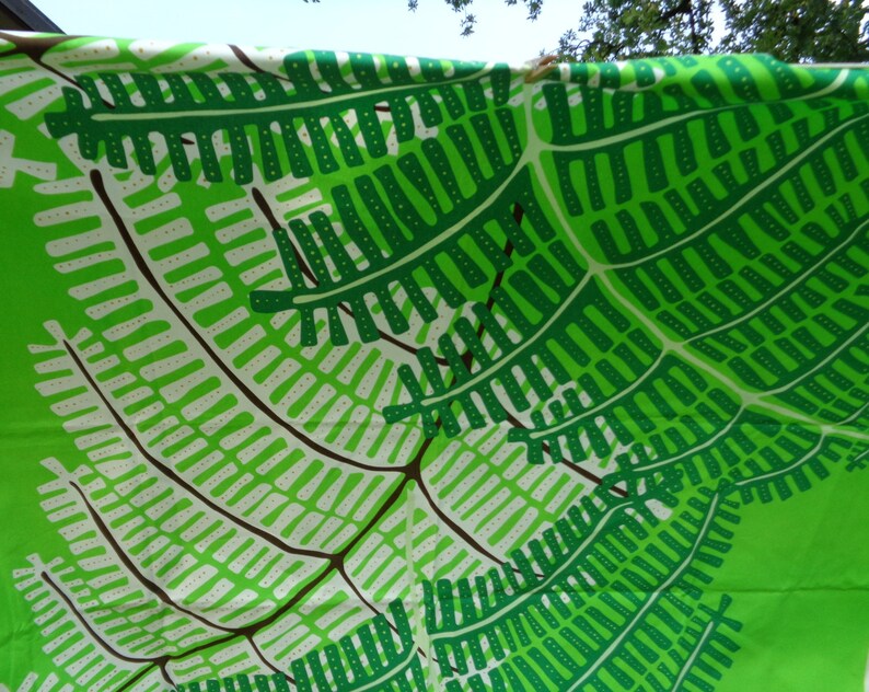 May include: A bright green fabric featuring a repeating pattern of fern leaves in green, white, and brown. The design creates a sense of depth and movement, suitable for home decor or clothing.