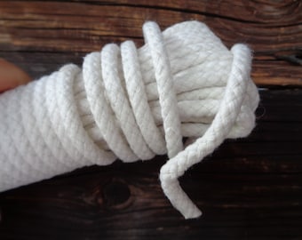 May include: A close-up of a white cotton rope coiled on a wooden surface. The rope is thick and has a natural, unbleached colour.