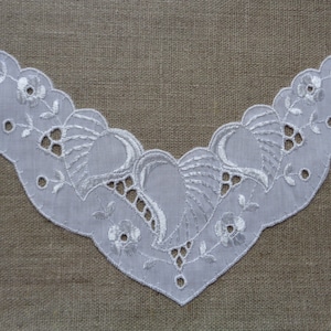 May include: White cotton lace trim with a scalloped edge and a delicate floral design. The lace has a V-shape and is perfect for adding a touch of elegance to any project.