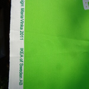May include: Vibrant green fabric with a white border. The border displays the text "Design: Maria Vinka 2011" and "IKEA of Sweden AB" in green. The fabric has a textured finish.