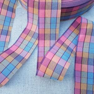 May include: A close-up of a plaid ribbon with pink, blue, yellow, and brown stripes. The ribbon is woven and has a soft, textured feel.