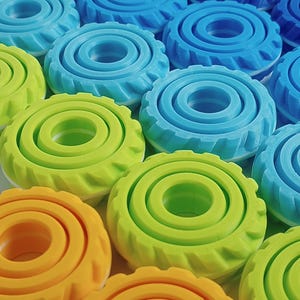 May include: A set of colorful, concentric circle-shaped toys with a textured outer edge. The toys are arranged in a gradient from blue to green to orange.
