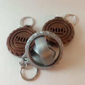 May include: Two brown wooden keychains with the number "906" engraved on them and a silver metal fidget spinner keychain.