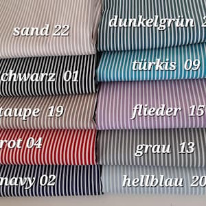 Puede incluir: Una pila de muestras de tela a rayas en varios colores, incluyendo arena, negro, topo, rojo, azul marino, verde oscuro, turquesa, lila, gris y azul claro. Cada tela tiene rayas blancas verticales y un nombre de color con un número.