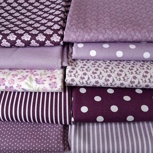 Pode incluir: Uma coleção de tecidos dobrados em vários tons de roxo e lavanda. Os padrões incluem pequenas bolinhas brancas sobre roxo escuro, listras verticais brancas finas sobre roxo claro, estampas florais e tecido roxo claro de cor sólida.