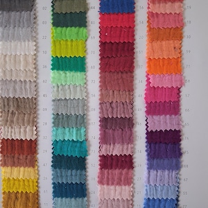 Op de afbeelding: Een stoffenkleurenkaart met vijf verticale kolommen van getextureerde dubbele gaasstofstalen in diverse kleuren. Elk staal is genummerd. De tekst bevat Article 9959, Quality Double Gauze, 100% CO, 125 GM2, Width 135 CM / 50 M en wasinstructies.