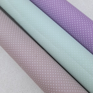 May include: Three rolls of fabric with white polka dots on different colored backgrounds: brown, light green, and purple.