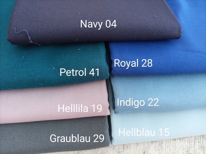 May include: A stack of fabric swatches in various shades of blue, green, and purple. The swatches are labeled with names and numbers, including Navy 04, Royal 28, Indigo 22, Hellblau 15, Graublau 29, Helllila 19, and Petrol 41.