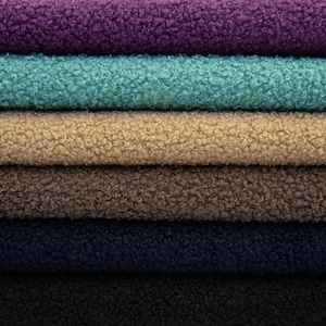 May include: A stack of six folded pieces of sherpa fleece fabric in various colors. The layers from top to bottom are purple, turquoise, beige, brown, navy blue, and black. Each piece features a thick, textured, and curly pile surface.