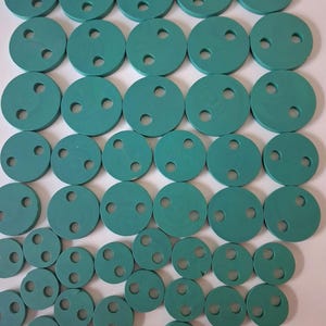 May include: A collection of teal-colored, circular rubber gaskets with three evenly spaced holes. The gaskets vary in size, arranged in a grid pattern. The image shows a variety of sizes, suitable for different applications.