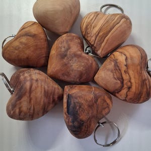 Peut inclure: Un ensemble de sept porte-clés en forme de cœur sculptés dans du bois poli, présentant chacun un motif de grain naturel distinct dans des tons de brun clair à foncé. Chaque cœur en bois est fixé à un anneau porte-clés en métal argenté.