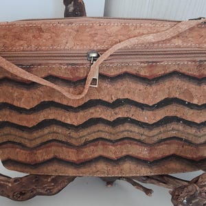 May include: A small, brown cork handbag with a black and brown wavy pattern. The bag has a zipper closure and a strap.
