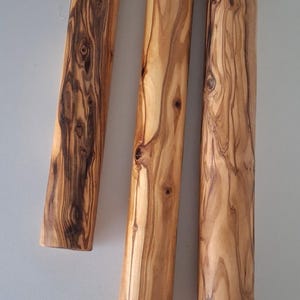 May include: Three cylindrical wooden candle holders with a natural wood grain pattern, suspended by a light-colored rope. The wood grain varies in intensity across the candle holders.