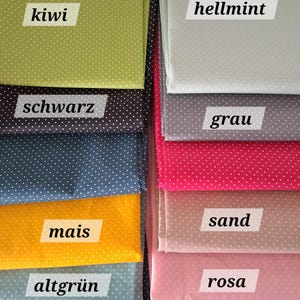 Könnte beinhalten: Eine Sammlung gefalteter Stoffmuster in verschiedenen Farben, jeweils mit weißen Punkten. Zu den Farben gehören Kiwi, Hellmint, Grau, Rosa und andere. Jedes Stoffmuster hat ein Etikett mit seinem Farbnamen.