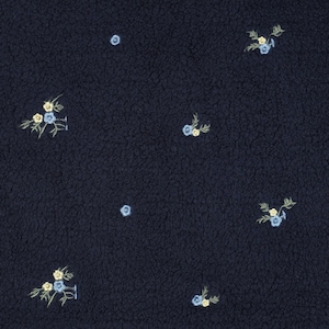 Puede incluir: Una tela azul marino oscuro con una superficie texturizada similar al forro polar. El material presenta un patrón repetitivo de pequeños grupos de flores bordadas que consisten en pétalos azul claro y amarillo pálido con tallos verdes.