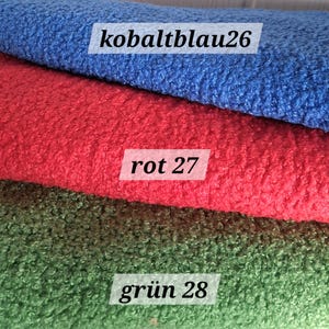 Könnte beinhalten: Drei Lagen strukturierten Stoffes, die horizontal übereinander liegen. Die oberste Lage ist blau mit dem Text kobaltblau26, die mittlere Lage ist rot mit dem Text rot 27 und die untere Lage ist grün mit dem Text grün 28. Das Material ist flauschig.