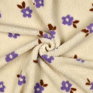 Puede incluir: Una tela de forro polar sherpa de color crema con un patrón repetitivo de pequeñas flores moradas con tallos y hojas marrones. El material tiene una superficie de pelo grueso, texturizado y esponjoso, reunido en un remolino central.