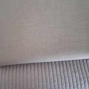 Könnte beinhalten: Nahaufnahme von zwei Stoffmustern. Der obere Stoff ist ein glattes, hellbeige Leinen. Der untere Stoff ist ein Cord mit vertikalen Rippen, in einer ähnlichen hellbeigen Farbe. Die Stoffe sind übereinander gestapelt.