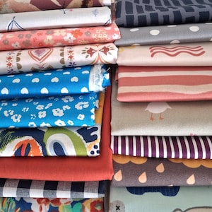 Könnte beinhalten: Ein Stapel gefalteter Stoffballen mit verschiedenen Mustern, darunter blaue Herzen, weiße Blumen, geometrische Formen, Streifen, Punkte und Tiermotive in Farben wie Blau, Rosa, Orange, Grau und Weiß, angeordnet in zwei vertikalen Spalten.