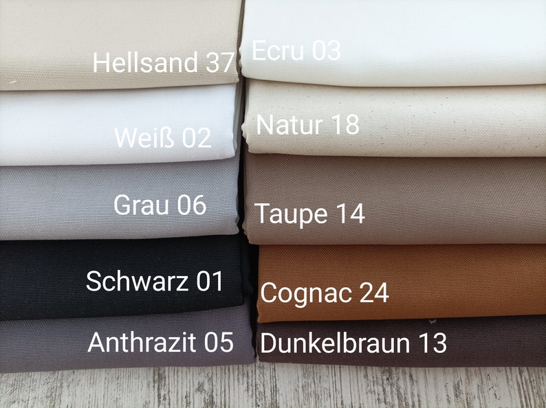 May include: A stack of fabric swatches in various shades of brown, gray, black, and white. The swatches are labeled with German names and numbers, such as "Hellsand 37", "Ecru 03", "Natur 18", "Wei&szlig; 02", "Grau 06", "Taupe 14", "Schwarz 01", "Cognac 24", "Anthrazit 05", and "Dunkelbraun 13".
