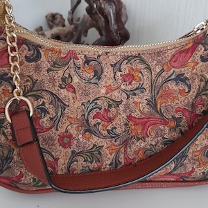May include: A small brown handbag with a floral pattern and a gold chain strap. The bag has a zipper closure and a brown leather strap.