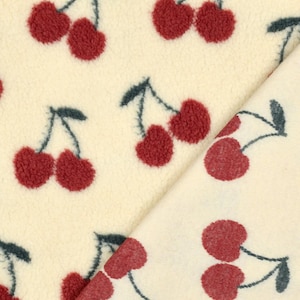 Könnte beinhalten: Ein cremefarbener Stoff mit einem sich wiederholenden Muster aus dunkelroten Kirschen mit dunkelgrünen Stielen und Blättern. Das Material hat auf der linken Seite eine weiche, flauschige, fleeceartige Textur und rechts eine glattere Webstruktur.