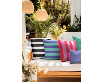 May include: Five striped throw pillows on a wooden bench. The pillows are in black and white, teal and white, pink and white, purple and white, and green. The bench is made of wood and has a white cushion.