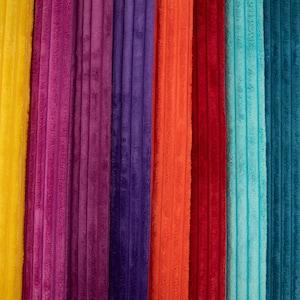 Op de afbeelding: Een verzameling verticale stroken stof met een zachte, geribbelde textuur. De kleuren van links naar rechts zijn heldergeel, magenta, dieppaars, levendig oranje, donkerrood, licht turquoise en een diepe kleur blauwgroen.