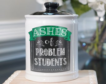May include: White ceramic jar with a black lid. The jar has a green and white chalkboard-style design with the text "Ashes of Problem Students".