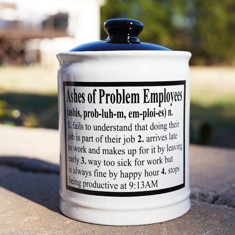 May include: White ceramic jar with a black lid. The jar has a black label with the text "Ashes of Problem Employees (ashis, prob-luh-m, em-ploi-es) n. 1. fails to understand that doing their job is part of their job 2. arrives late to work and makes up for it by leaving early 3. way too sick for work but is always fine by happy hour 4. stops being productive at 9:13AM"