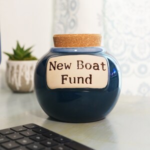 May include: A blue ceramic jar with a cork lid and a white label that reads "New Boat Fund".