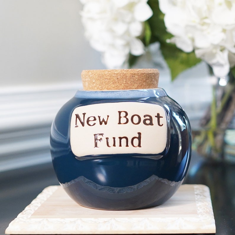 May include: A blue ceramic jar with a cork lid and a white label that reads "New Boat Fund".
