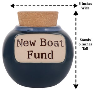 May include: Blue ceramic money box with a cork lid. It has a white label that says "New Boat Fund". The box stands 6 inches tall and is 5 inches wide.