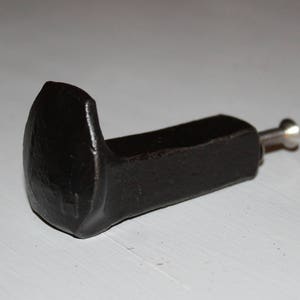 May include: A black metal hook shaped like a nail with a silver screw. The hook is designed for hanging items on a wall.