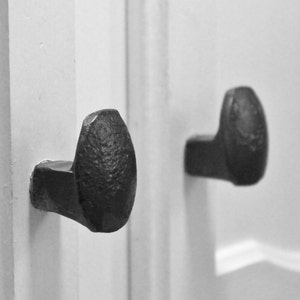 May include: Two black metal door handles with a textured finish. The handles are attached to a white door.