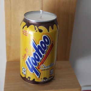 May include: A yellow and blue Yoohoo chocolate drink can candle. The can has a brown chocolate drip design and the text "Shake It!" and "Chocolate Drink" on it.