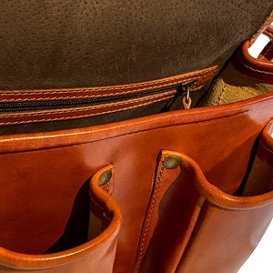 May include: A brown leather messenger bag with multiple pockets and a zippered closure. The bag is open and the inside is lined with a light brown fabric.