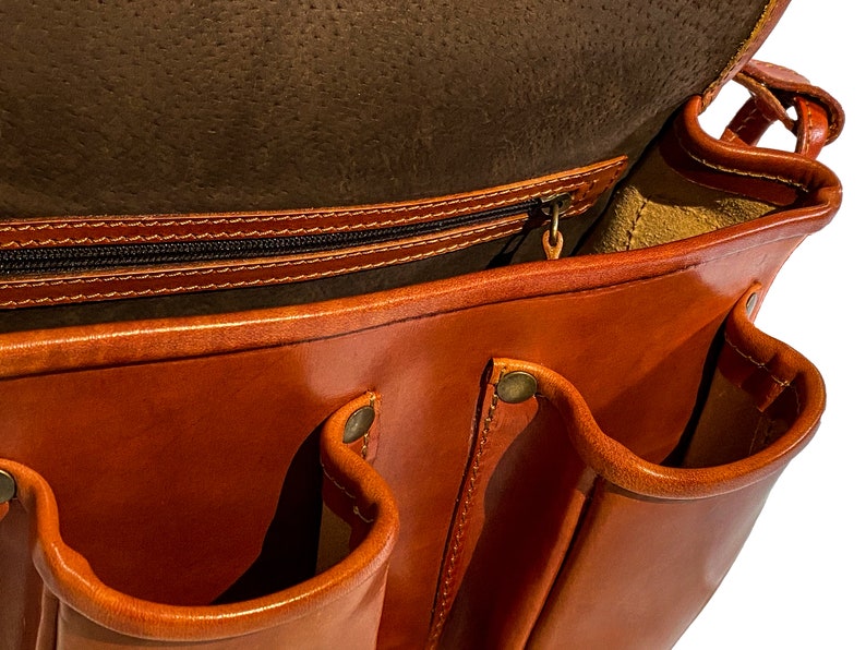 May include: A brown leather messenger bag with multiple pockets and a zippered closure. The bag is open and the inside is lined with a light brown fabric.