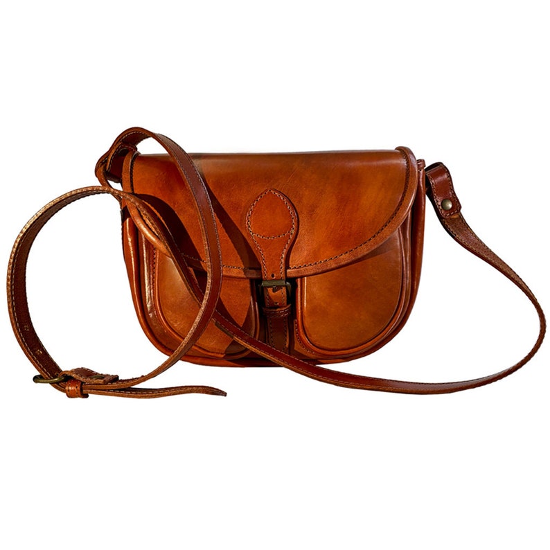 May include: A brown leather satchel bag with a flap closure and a buckle. The bag has a single strap and a small pocket on the front.