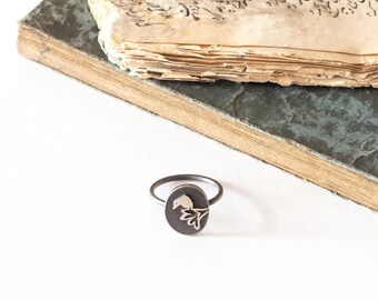 May include: A silver ring with a delicate floral design. The ring is on a white surface next to an old book.