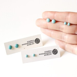 May include: Two pairs of turquoise blue stud earrings on white cards with the text "Zohreh Khodaparast Jewelry".