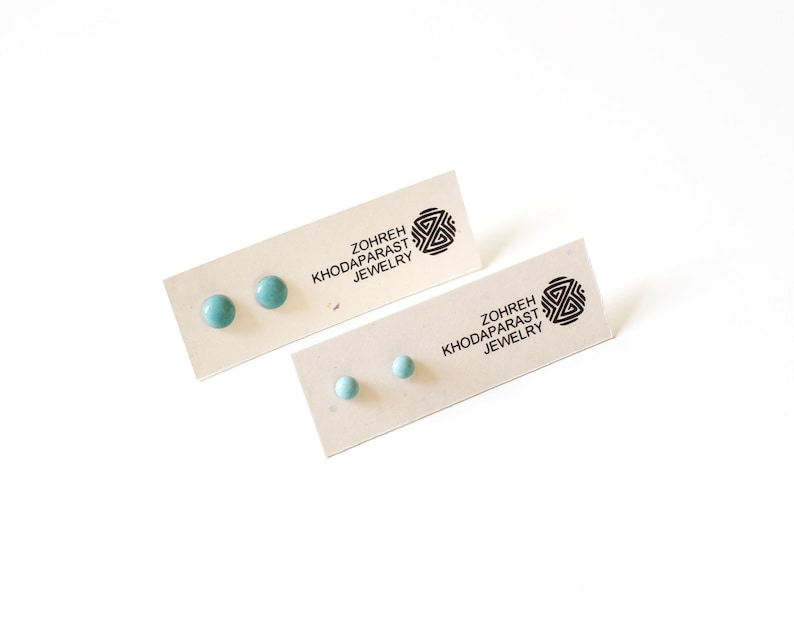 May include: Two pairs of teal blue ceramic stud earrings displayed on a card with the text "Zohreh Khodaparast Jewelry".