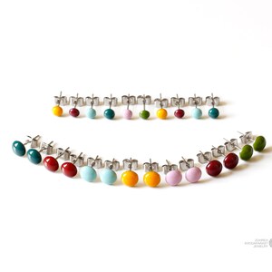 May include: A set of 18 colorful enamel stud earrings. The earrings are arranged in a semi-circle pattern on a white background. The colors include red, orange, yellow, green, blue, and purple.
